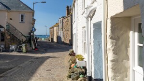 Une rue pavée bordée de bâtiments des deux côtés, un escalier menant à un niveau supérieur et une vue dégagée sur la mer au loin.