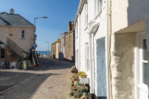 Une rue pavée bordée de bâtiments des deux côtés, un escalier menant à un niveau supérieur et une vue dégagée sur la mer au loin.