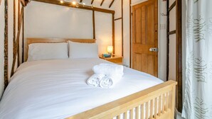 A neatly made bed with white linens and a rolled towel, a wooden headboard, and a nightstand with a lamp. - 2 Bed in St Ives (oc-cotsp) (Saint Ives)