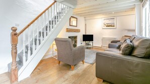 A living room with a staircase, a grey armchair, a brown sofa, a flat-screen TV, and a radiator. - 2 Bed in St Ives (oc-cotsp) (Saint Ives)