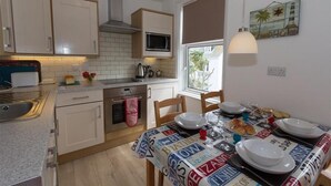 Een kleine keuken met een magnetron, oven en spoelbak. Een eettafel is gedekt met borden, glazen en een menukaart.