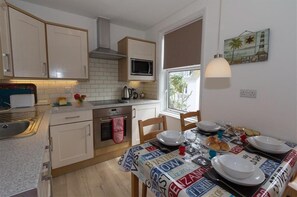 A compact kitchen with a microwave, oven, and sink. A dining table is set with plates, glasses, and a menu. - 2 Bed in St Ives (oc-ven10a) (Saint Ives)