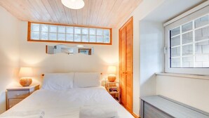 A bedroom with a large bed, wooden headboard, two bedside lamps, a wooden wardrobe, and a window. - 1 Bed in St Ives (oc-crab01) (St Ives)