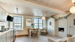 A coastal interior with a dining area, kitchen, and living space, featuring wooden ceilings and large windows. - 1 Bed in St Ives (oc-crab01) (St Ives)