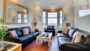 A living room with two black leather sofas, a wooden coffee table, and a large mirror. - 2 Bed in St Ives (oc-clv2a) (Saint Ives)