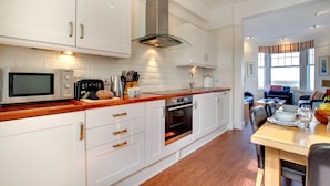 A modern kitchen with white cabinetry, a stainless steel range hood, a microwave, and an oven. - 2 Bed in St Ives (oc-clv2a) (Saint Ives)