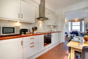 A modern kitchen with white cabinetry, a stainless steel range hood, a microwave, and an oven. - 2 Bed in St Ives (oc-clv2a) (Saint Ives)