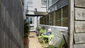 A narrow outdoor patio with a small table and chairs, a potted plant, and a door leading to a building. - 2 Bed in St Ives (oc-clv2a) (Saint Ives)