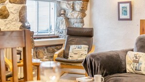 Un mur de pierre, un fauteuil en cuir, une table en bois et un canapé dans une pièce chaleureuse.