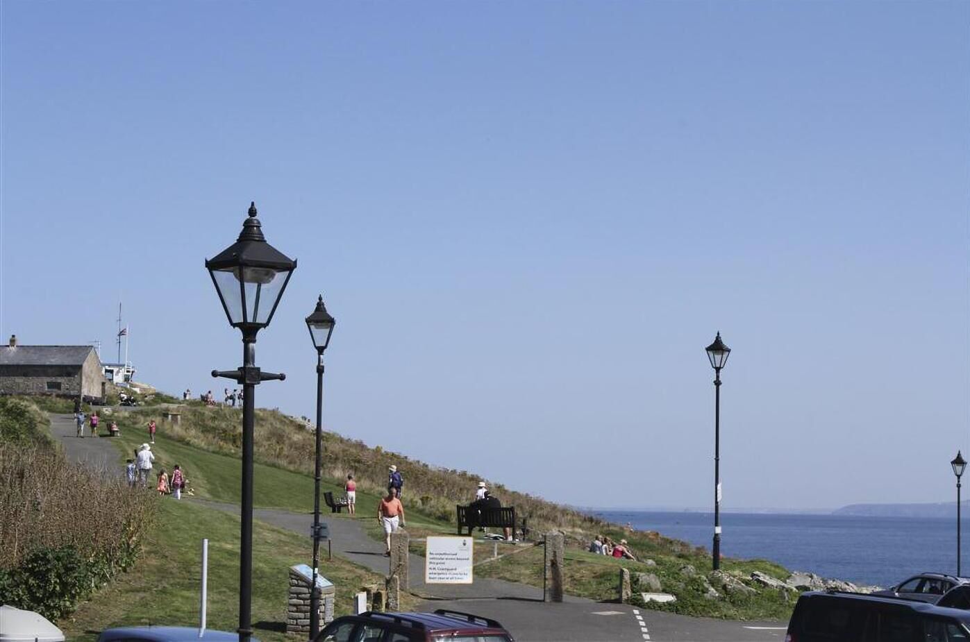 A coastal path with street lamps, a sign, and people walking.