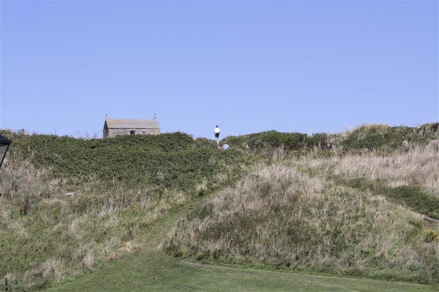 Eine Wiese mit einem Steinhaus und einer Person, die auf einem Hügel steht.
