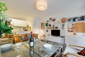 A modern kitchen with white cabinets, a dining area with a glass table, and a living space with a TV and decorative items. - 2 Bed in St Ives (oc-redc4) (Saint Ives)