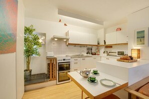 A modern kitchen with white cabinetry, a built-in oven, a stove, and a dining area with a table set for two. - 2 Bed in St Ives (oc-redc4) (Saint Ives)