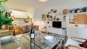 Eine moderne Küche mit weißen Schränken, ein Essbereich mit Glastisch und ein Wohnzimmer mit Fernseher und Dekoration.
