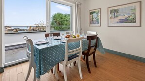 Een eetgedeelte met een tafel voor twee, uitzicht op de zee door grote ramen, en twee inlijste landschapsprenten aan de muur.