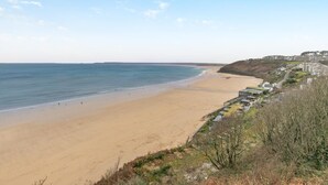 A coastal beach with a sandy shore, a clear sky, and buildings along the coastline. - 2 Bed in St Ives (oc-godct7) (Carbis Bay)