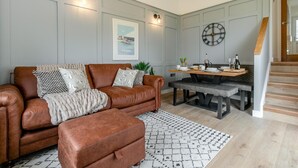 A modern living room with a leather sofa, a coffee table, and a dining area with a wooden table and bench. - 2 Bed in St Ives (oc-godct7) (Carbis Bay)