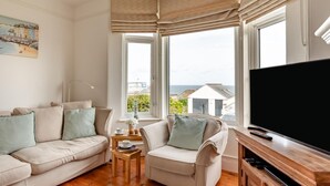 Un salón con sofá, sillón, televisor y ventanas con vistas.