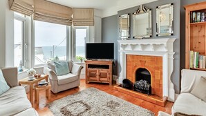 Una sala de estar con chimenea, televisor y vista al mar.