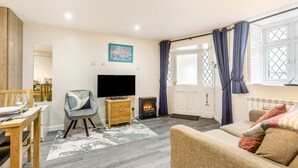 Ein Wohnzimmer mit Sofa, Fernseher, Kamin, Essbereich und Blick durch ein Fenster.