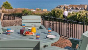 A table set outdoors with a scenic view of the ocean and a person walking in the background. - 2 Bed in St. Ives (oc-lyon09) (Saint Ives)