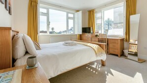 A hotel room with a large bed, a desk, a chair, a TV, and a window with curtains. - 2 Bed in St. Ives (oc-lyon09) (Saint Ives)