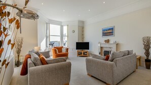 A modern living room with two grey sofas, a small orange armchair, and a television. - 2 Bed in St. Ives (oc-lyon09) (Saint Ives)