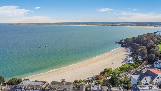 A coastal view with a sandy beach, clear blue water, and a residential area with houses and greenery. - 2 Bed in St. Ives (oc-lyon09) (Saint Ives)