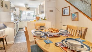 A dining area with a table set for four, kitchen in the background, and a beach-themed wall decoration. - 2 Bed in St Ives (oc-killa) (St Ives)