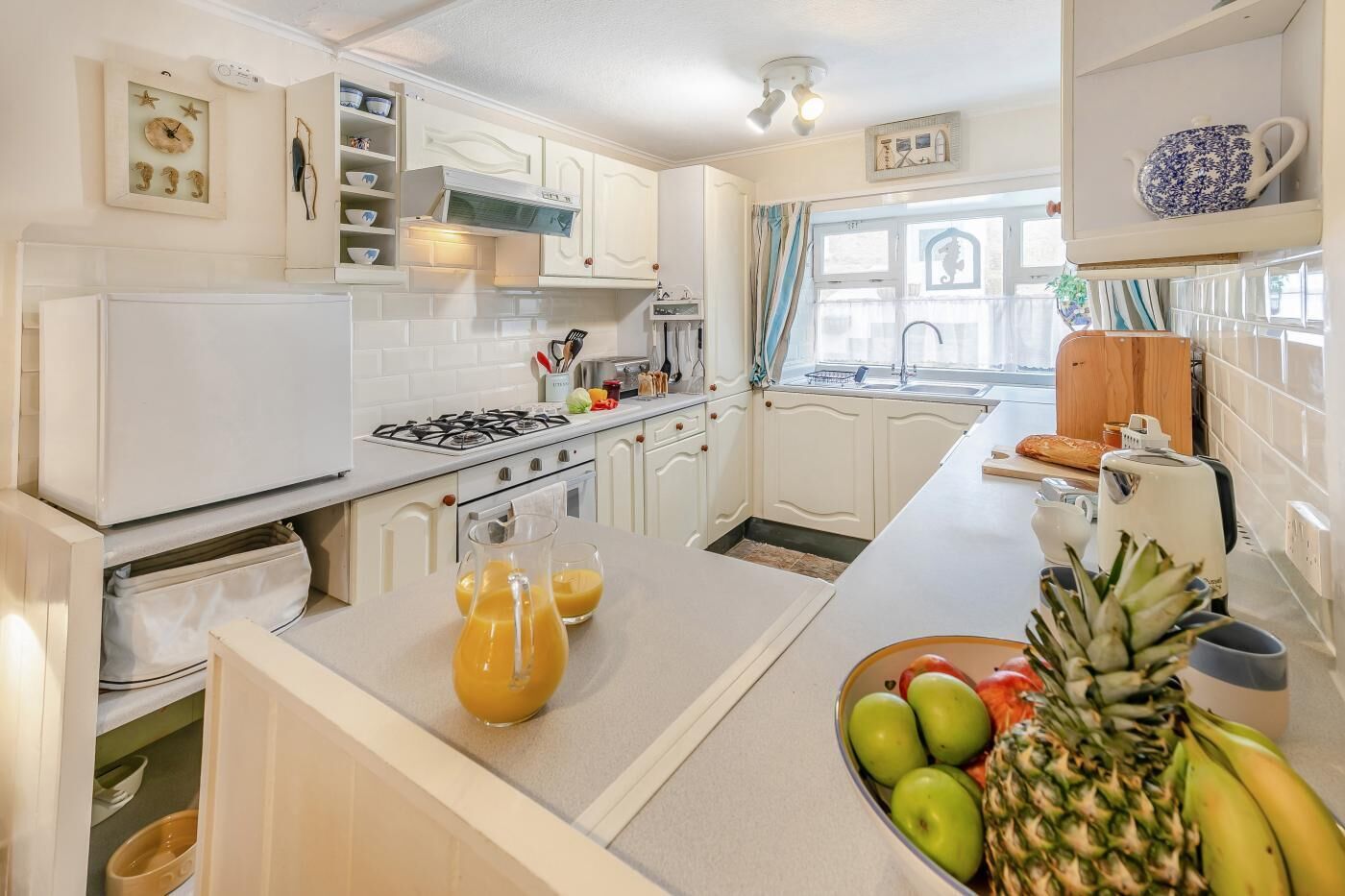 Een keuken met witte kastjes, een fornuis, een spoelbak en een raam met gordijnen.