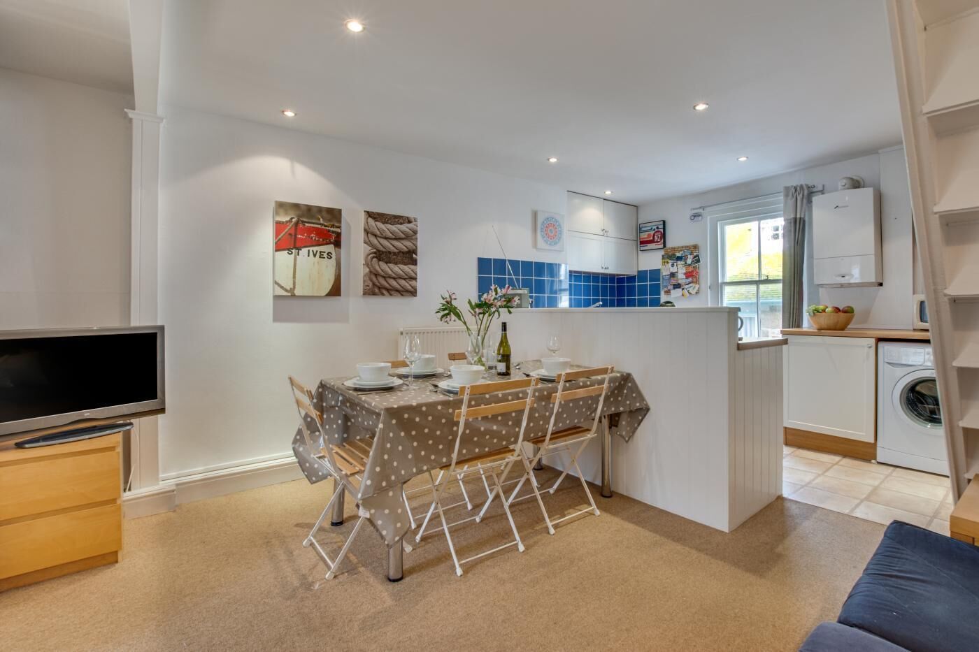 A compact kitchen with a dining area, a washing machine, and a TV.