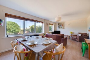 Un coin repas avec une table dressée pour quatre personnes, un canapé marron et un téléviseur en arrière-plan.