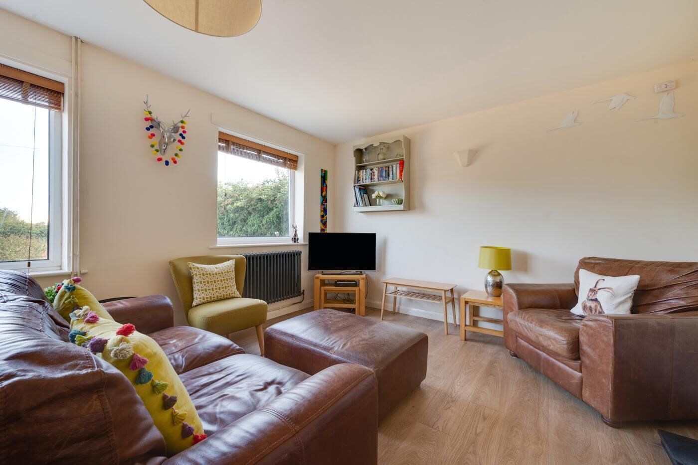 Una sala de estar con un sofá de cuero marrón, un sillón verde, una mesa de centro de madera, un televisor y una estantería.