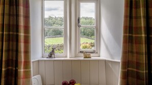 Ein Zimmer mit zwei Fenstern, einem Heizkörper, einem kleinen Tisch mit Äpfeln und einer Hundefigur.