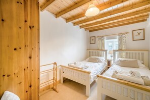 Une chambre avec deux lits simples, des têtes de lit en bois, un plafond en bois et une fenêtre avec des rideaux.