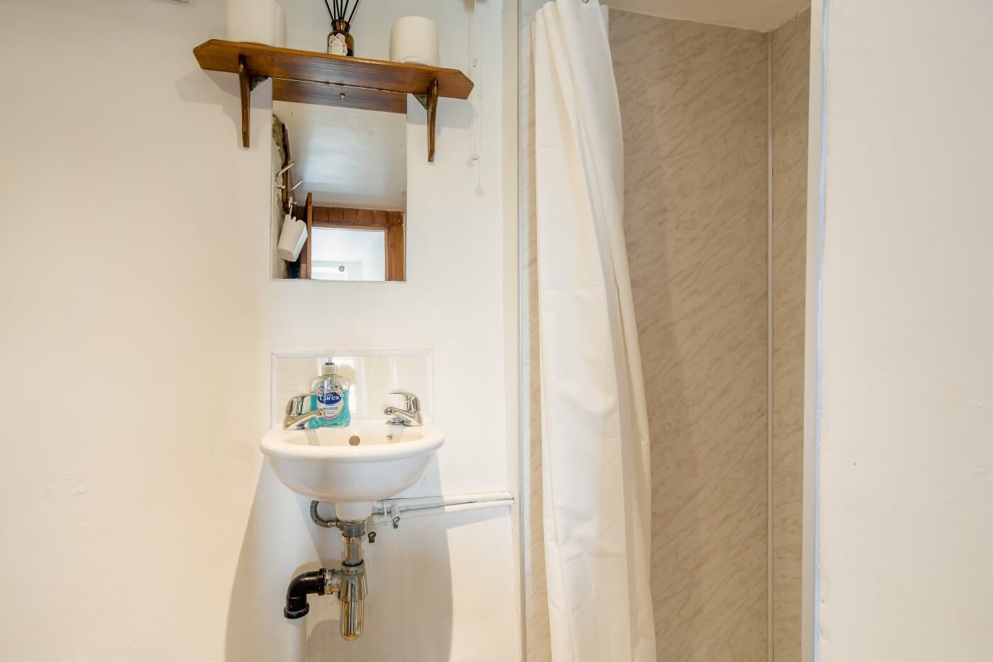 Une salle de bain avec un lavabo blanc, un miroir et un rideau de douche.