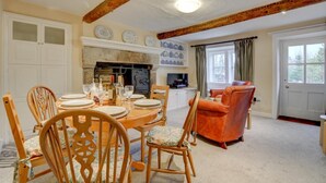 A dining area with a wooden table set for four, surrounded by wooden chairs. A fireplace is visible in the background, and there is a television on a cabinet. - 3 Bed in Horton-in-Ribblesdale (oc-ds933) (Horton in Ribblesdale)