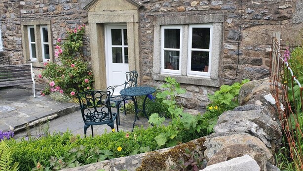 A stone building with a door, windows, and a small garden area with a table and chairs. - 3 Bed in Horton-in-Ribblesdale (oc-ds933) (Horton in Ribblesdale)