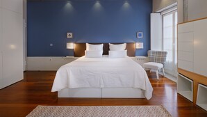 A bedroom with a large bed, wooden ceiling beams, a blue accent wall, and a white chair. - Design Studio for 3 in City Center (Oporto)