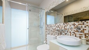 A modern bathroom with a glass-enclosed shower, a white toilet, and a sink with a mosaic backsplash. - Design Studio for 3 in City Center (Oporto)