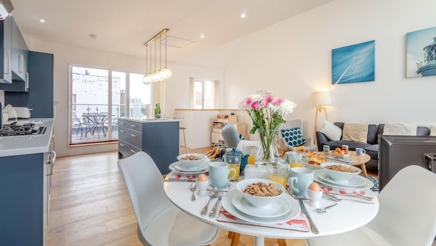 Une cuisine moderne avec un coin repas, une vue sur la ville et un salon comprenant un canapé et un tableau.