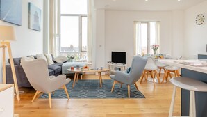 Un salon moderne comprenant un canapé, des fauteuils, un téléviseur et un coin repas avec une table et des chaises.