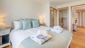 Un lit bien fait, avec des oreillers, une table de chevet avec une lampe, et une salle de bain visible à travers une porte ouverte.
