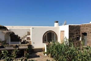 A courtyard with a white building, a stone wall, and a thatched-roof structure. - Holiday Home 'Dammuso Civulia Pantelleria' with Private Terrace, Wi-Fi and Air Conditioning (pantelleria)