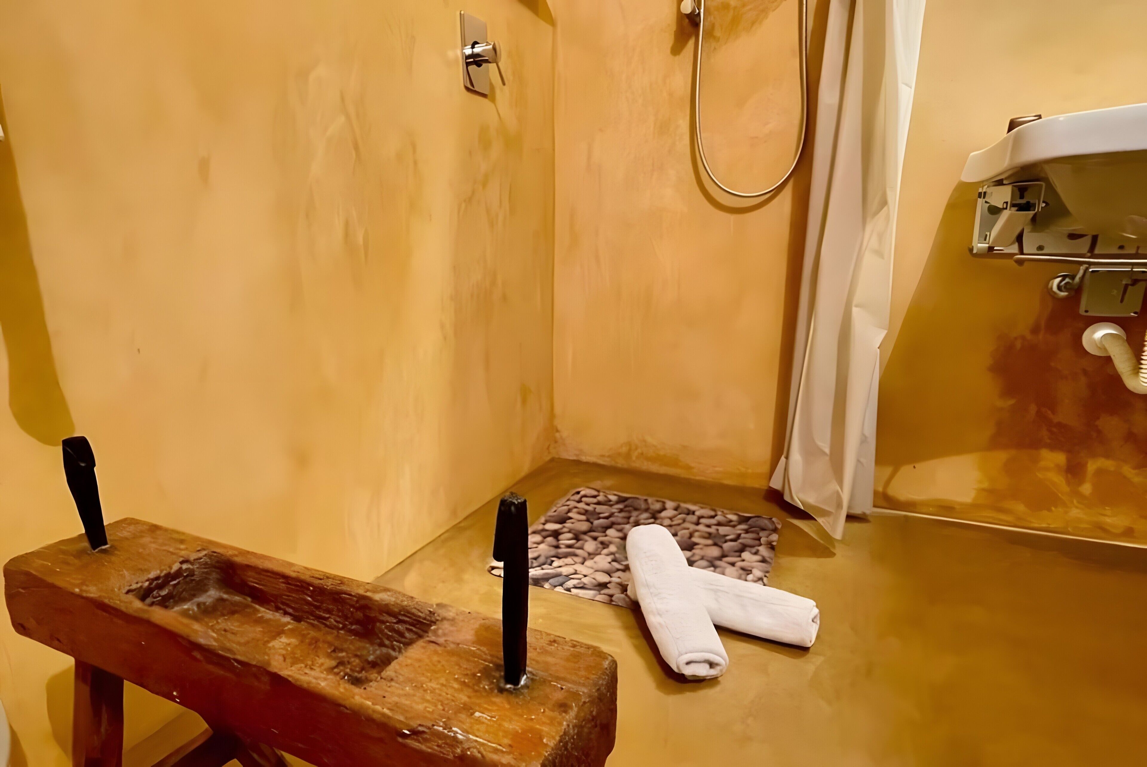 A bathroom with a wooden bench, a towel, a pebbled bath mat, and a shower area.