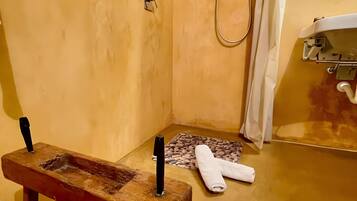A bathroom with a wooden bench, a towel, a pebbled bath mat, and a shower area.