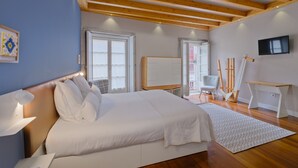 Une chambre avec un grand lit, des poutres en bois, une télévision et un bureau équipé de matériel de dessin.