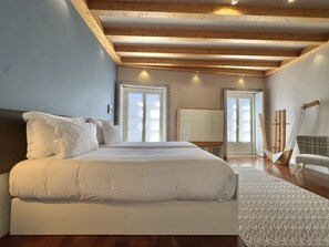 A bedroom with a large bed, wooden ceiling beams, a wardrobe, and a view through a door. - Stylish Studio with balcony for 3 in Taipas Center (Oporto)