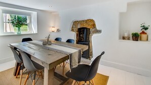 Uma sala de jantar com mesa de madeira rústica, cadeiras pretas, lareira de pedra e janela com vista para o verde.