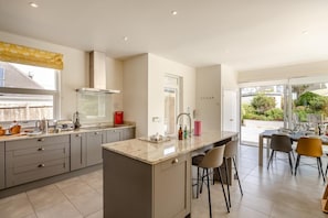 A modern kitchen with a central island, bar stools, and a dining area with a view. - 4 Bed in Newquay (oc-p00709) (Newquay)